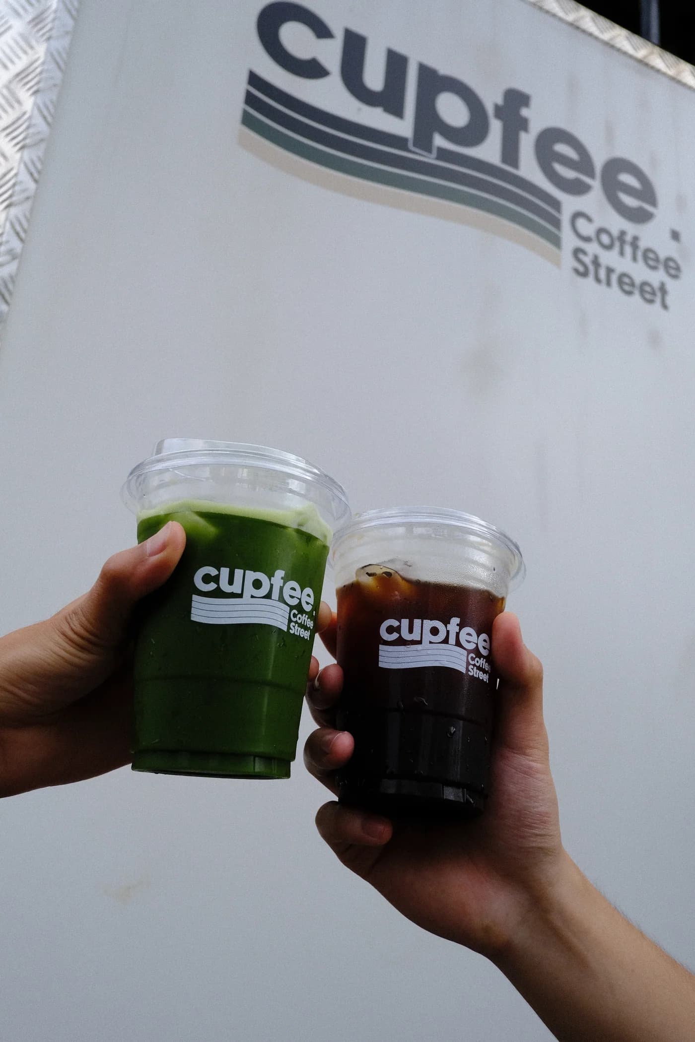 Cupfee matcha and iced coffee held in front of the shop logo
